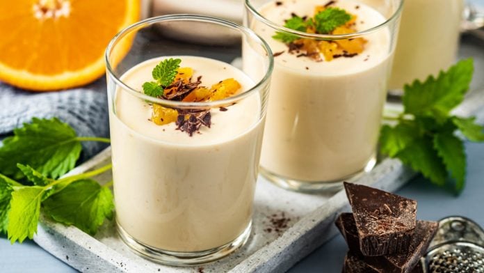 3 Gläser mit Topfencreme stehen auf einem Tablett, daneben Schokostreusel und eine Orange