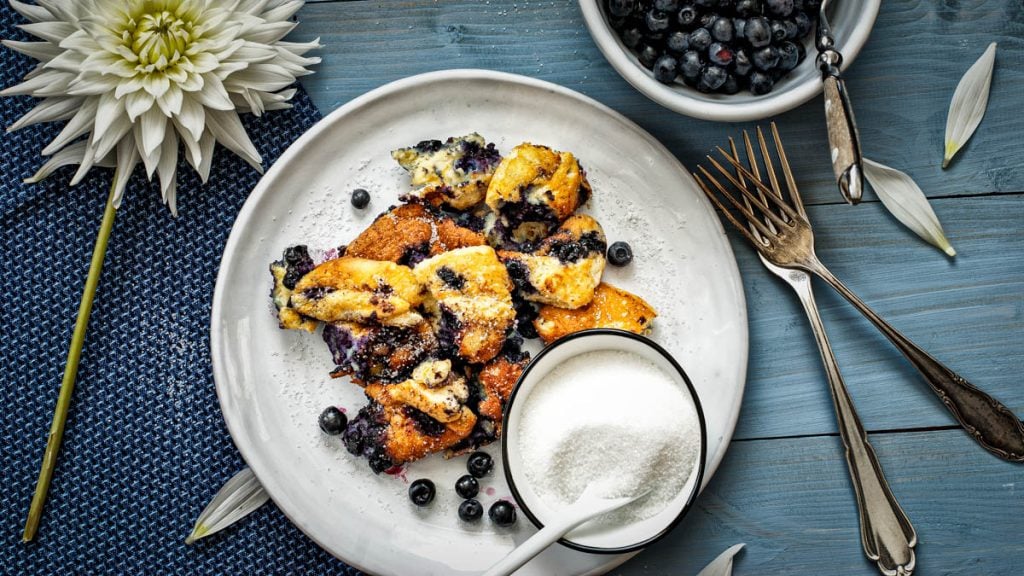 Schwarzbeerschmarrn auf einem Teller angerichtet mit Zucker und frischen Schwarzbeeren