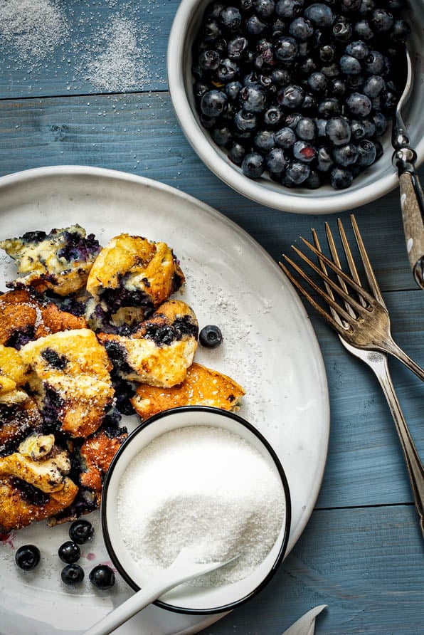 Schwarzbeerschmarrn auf einem Teller angerichtet mit Zucker und frischen Schwarzbeeren
