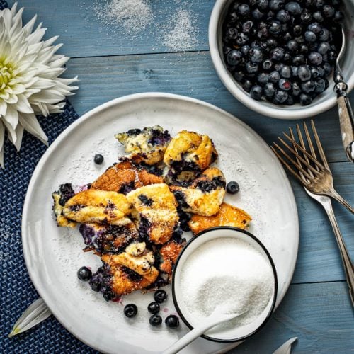 Heidelbeerschmarrn auf einem Teller angerichtet mit Zucker und frischen Heidelbeeren