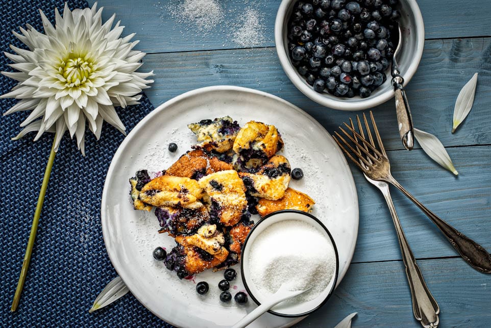 Heidelbeerschmarrn auf einem Teller angerichtet mit Zucker und frischen Heidelbeeren