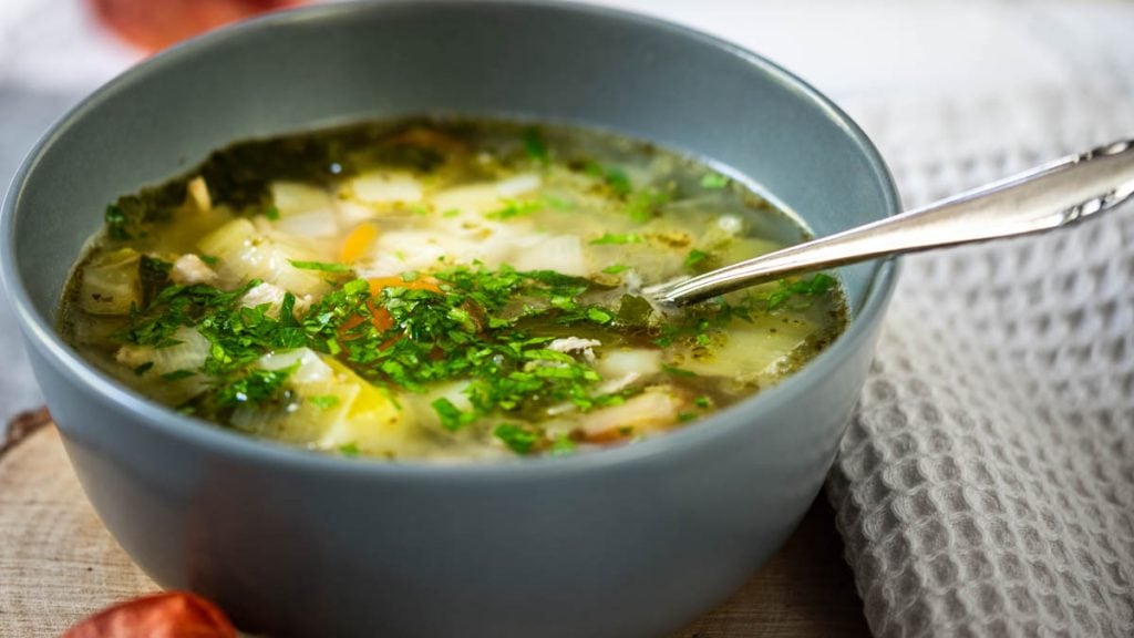 Eine Bowl mit Hühnersuppe steht auf einem Holzbrettchen