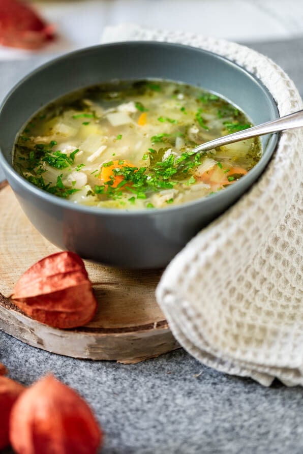 Eine Bowl mit Hühnersuppe steht auf einem Holzbrettchen