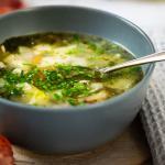 Eine Bowl mit Hühnersuppe steht auf einem Holzbrettchen