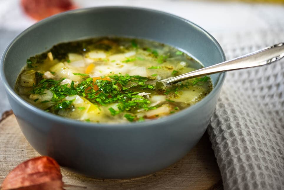 Eine Bowl mit Hühnersuppe steht auf einem Holzbrettchen