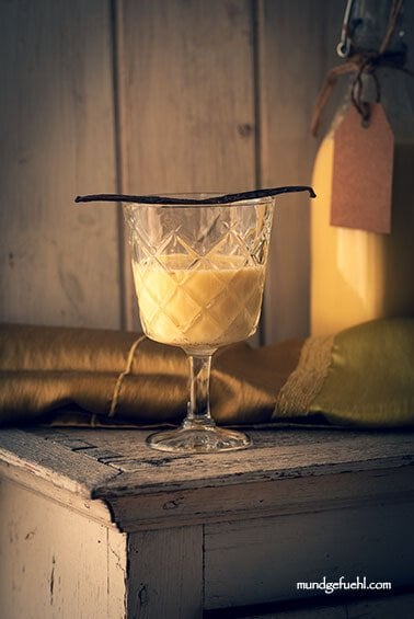 Ein Glas und eine Flasche Eierlikör stehen auf einem Kästchen mit weihnachtlicher Deko