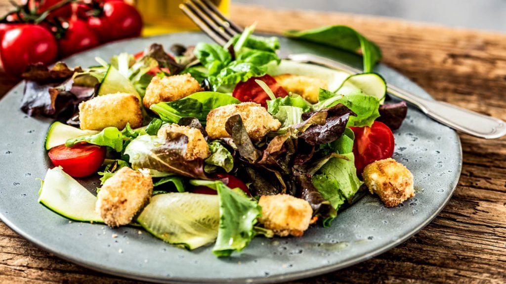 Bunter Salatteller mit gebackenem Schafskäse steht auf einem Tisch