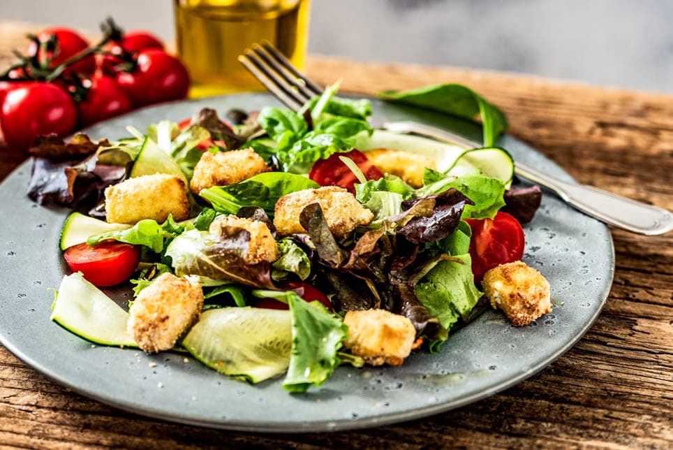 Bunter Salatteller mit gebackenem Schafskäse steht auf einem Tisch