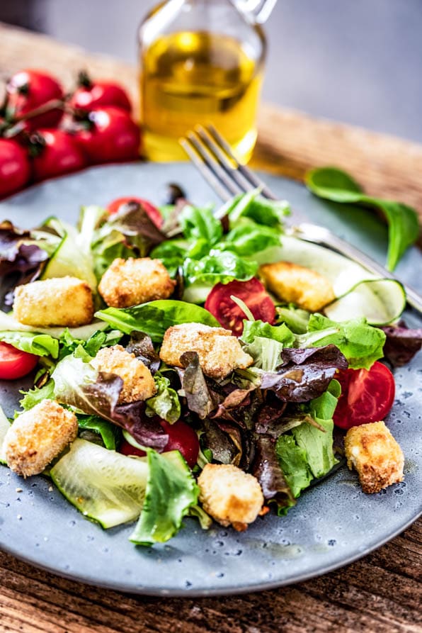 Bunter Salatteller mit gebackenem Schafskäse steht auf einem Tisch