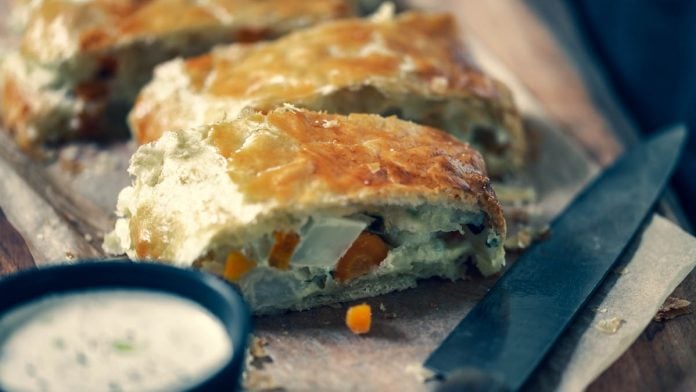 aufgeschnittener Gemüsetrudel auf Brett mit Sauce