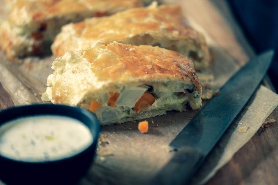 aufgeschnittener Gemüsetrudel auf Brett mit Sauce