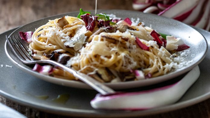 spaghetti-mit-gebratenem-radicchio-und-pinienkernen Ein Teller mit Spaghetti und gebratenem Radicchio steht am Tisch