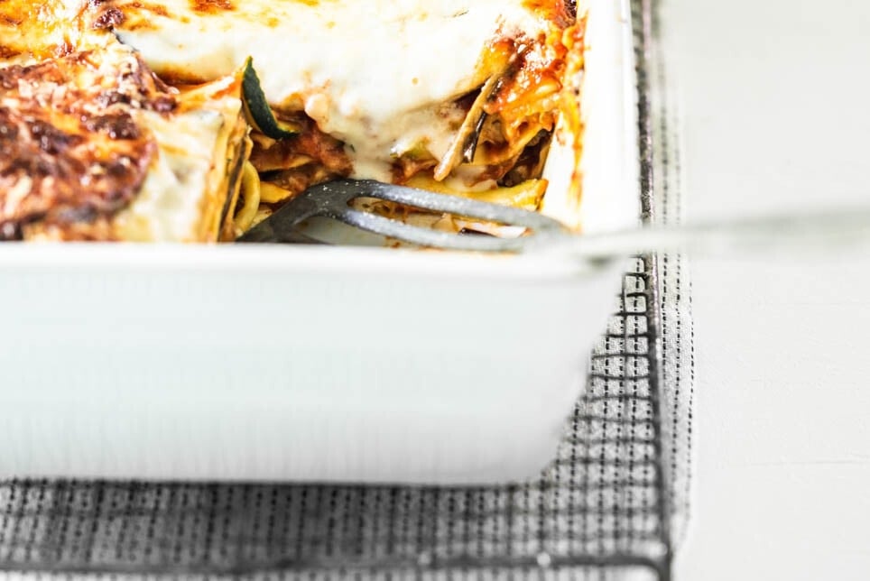 Auflaufform mit Gemüselasagne mit Zucchini und Aubergine steht auf einem Gitter