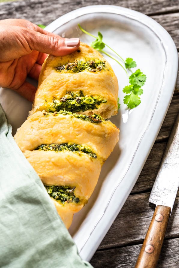 Eine Hand bricht ein Stück eines Kräuterbaguette ab