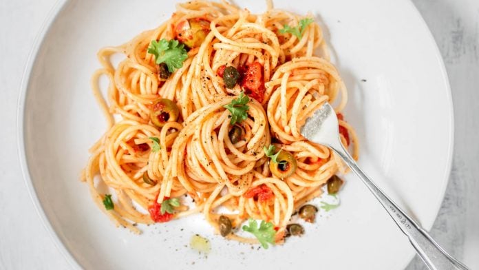 weißer Teller mit Spaghetti alla Puttanesca und einer Gabel