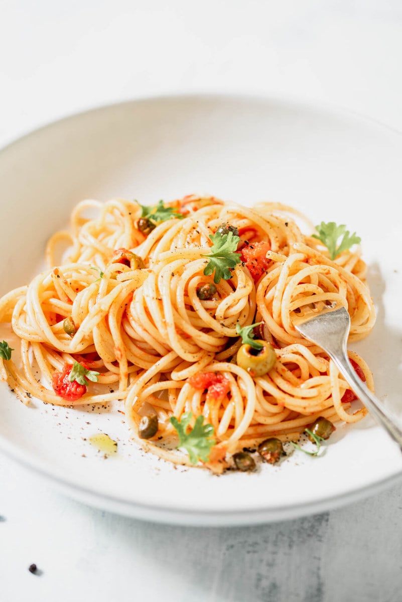 weißer Teller mit Spaghetti alla Puttanesca und einer Gabel