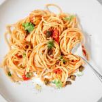 weißer Teller mit Spaghetti alla Puttanesca und einer Gabel