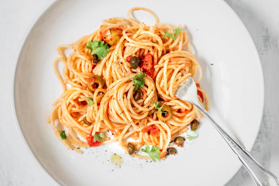 weißer Teller mit Spaghetti alla Puttanesca und einer Gabel