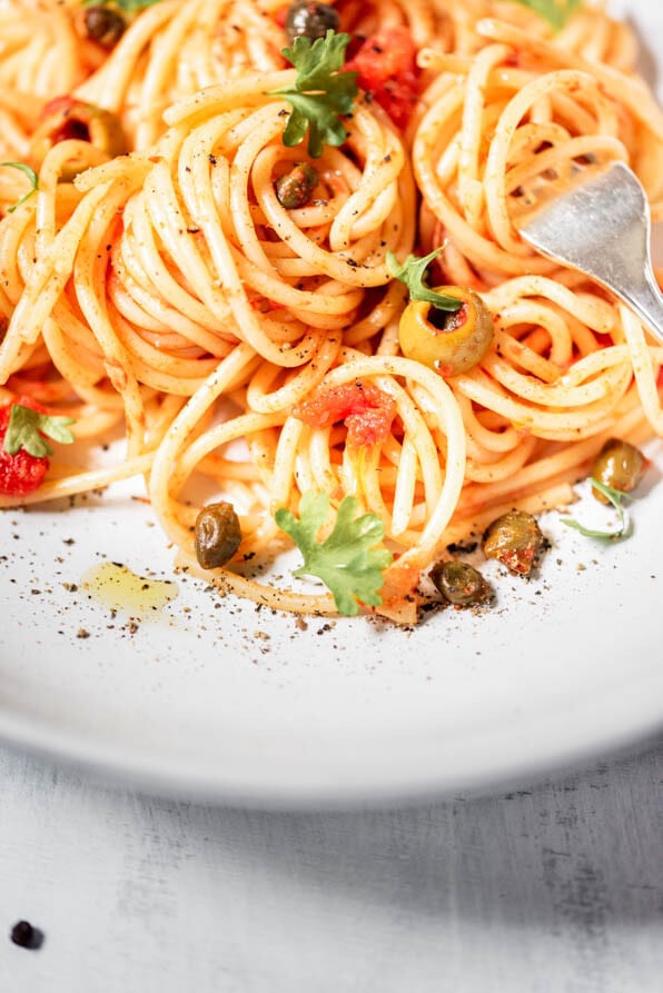 weißer Teller mit Spaghetti alla Puttanesca und einer Gabel
