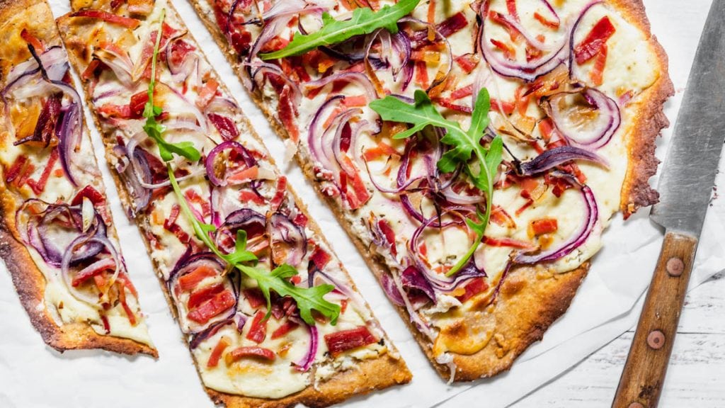 Flammkuchen Elsässer Art liegt aufgeschnitten auf Backpapier