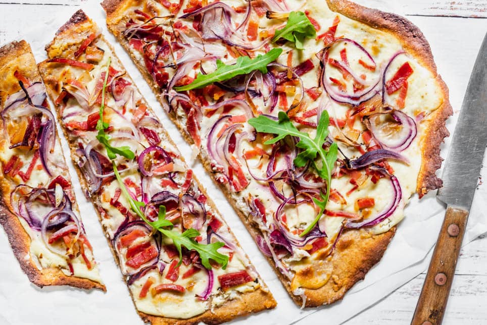 Flammkuchen Elsässer Art liegt aufgeschnitten auf Backpapier