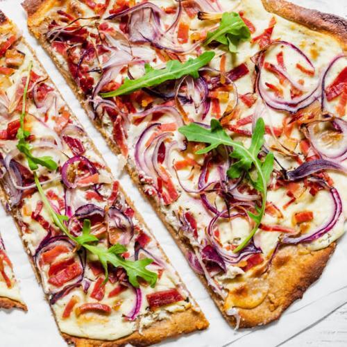 Flammkuchen Elsässer Art liegt aufgeschnitten auf Backpapier