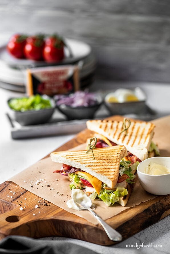 Club Sandwich ist mit Aioli auf einem Holzbrett angerichtet