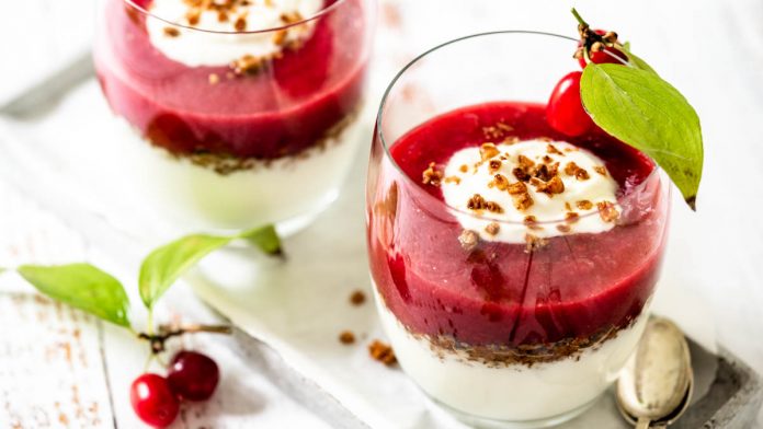 schichtdessert-aus-kornelkirschen-fruchtmus-und-joghurtcreme Zwei Dessertgläser mit Fruchtcreme stehen auf Tablett