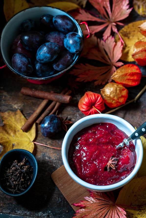 Eine Schale Pflaumenmarmelade steht neben einer Schale Pflaumen und herbstlicher Deko