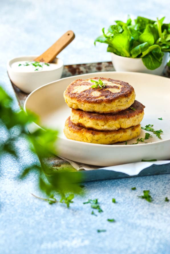 Topfenlaibchen auf einem Teller. Dahinter ein Dip und Salat