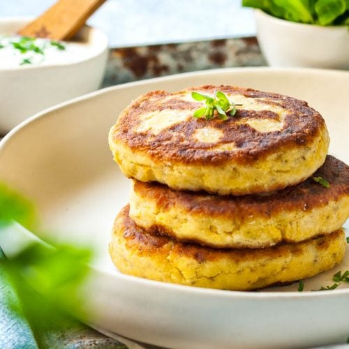 Topfenlaibchen auf einem Teller. Dahinter ein Dip und Salat