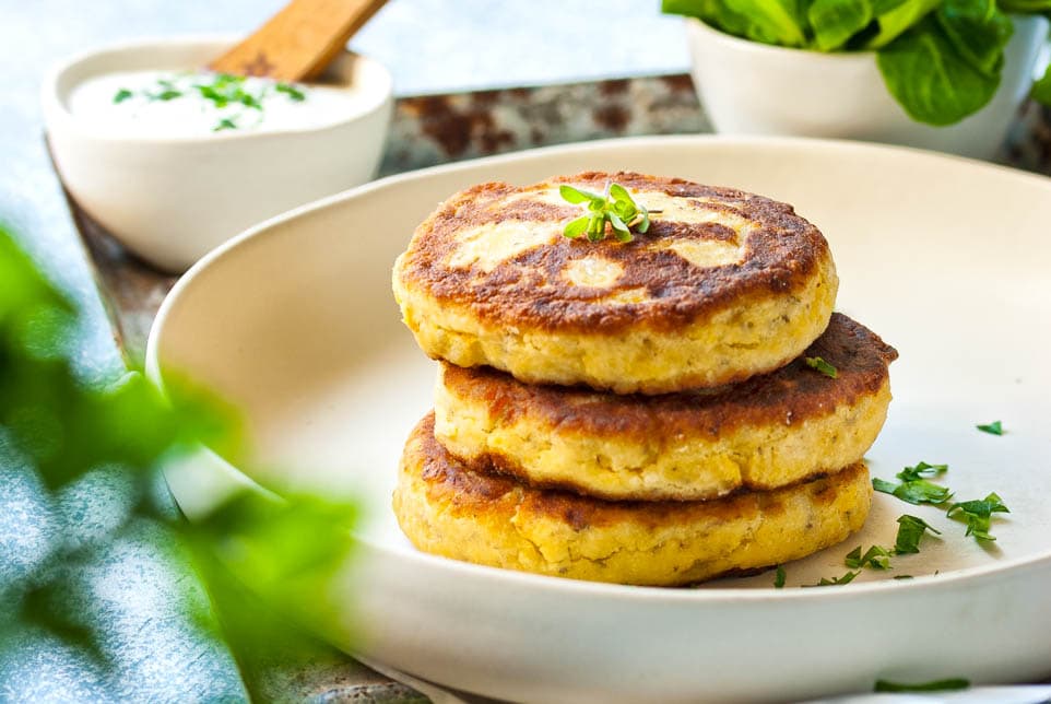 Topfenlaibchen auf einem Teller. Dahinter ein Dip und Salat