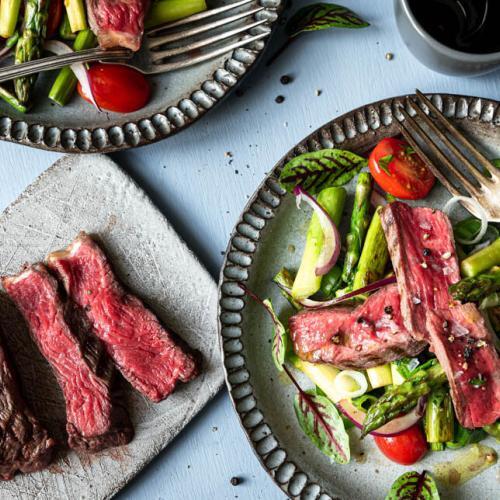 Spargelsalat mit aufgeschnittenem Rumpsteak auf einem Teller, daneben zartrote Rumpsteakscheiben