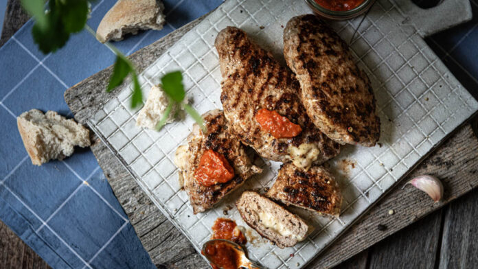 pljeskavica Aufgeschnittene Pljeskavica mit Ajvar auf Brett