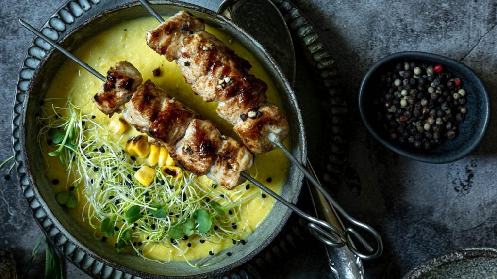 Maissuppe und zwei Putenspießen steht in Schüssel am Tisch