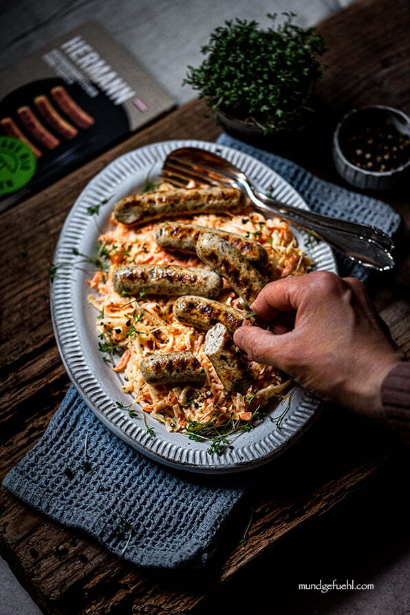 Jemand nimmt ein Rostbratwürstchen von einem Teller