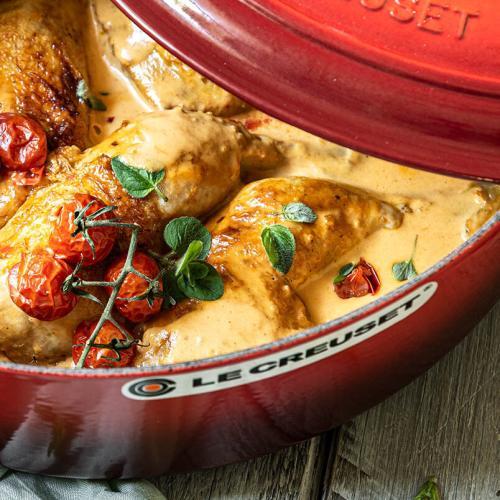 Huhn in einem Bräter mit Tomaten steht auf einem Tisch