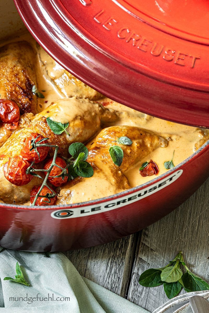 Huhn in einem Bräter mit Tomaten steht auf einem Tisch