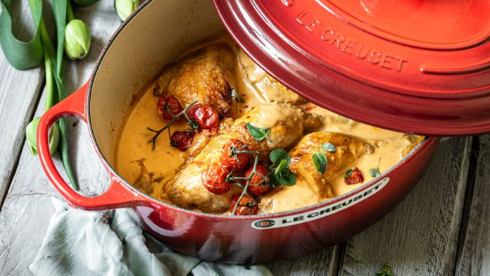 geschmortes-huhn-mit-ofentomaten-in-cheddarsauce Huhn in einem Bräter mit Tomaten steht auf einem Tisch