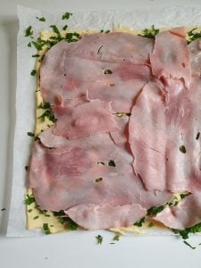 Pizzateig mit Schmelzkäse, Petersilie und Schinken belegt
