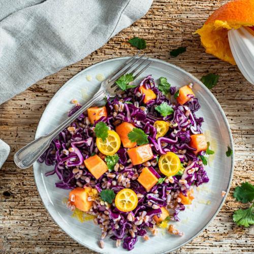 Rotkohlsalat mit Papaya auf einem Teller und Holztisch