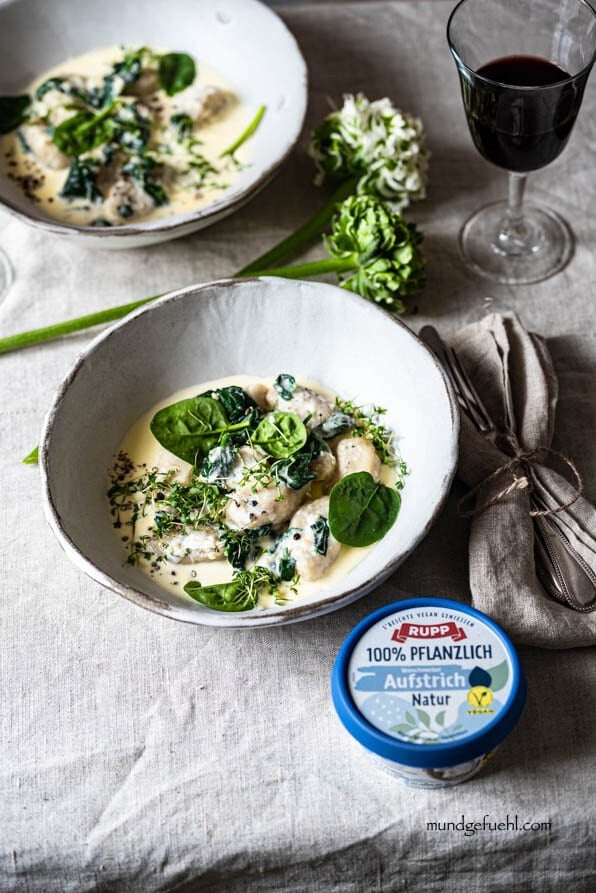 Vegane Gnudi mit Spinatrahm auf romantisch gedecktem Tisch mit Wein und Blumen