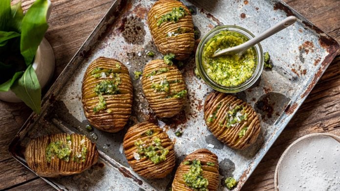 Hasselback Kartoffeln sind mit einem Glas Pesto auf einem Tablett