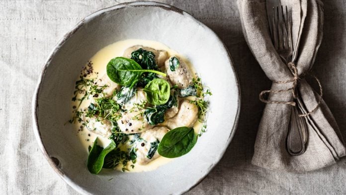 Vegane Gnudi mit Spinatrahm auf romantisch gedecktem Tisch mit Wein und Blumen