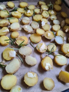 In Stücke geschnittene Kartoffeln auf einem Backblech mit Butter und Rosmarin