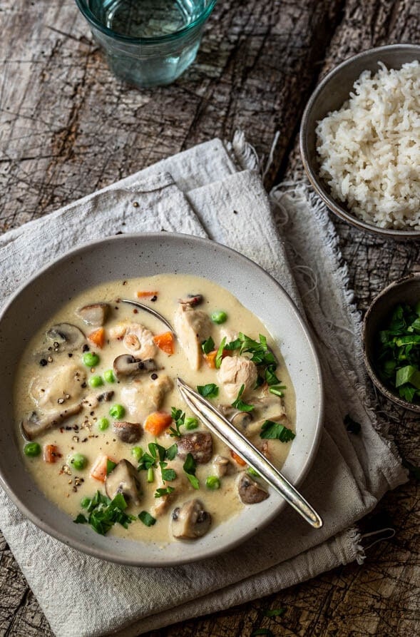 Ein Teller Hühnerfrikassee steht mit einer Schale Reis auf dem Tisch