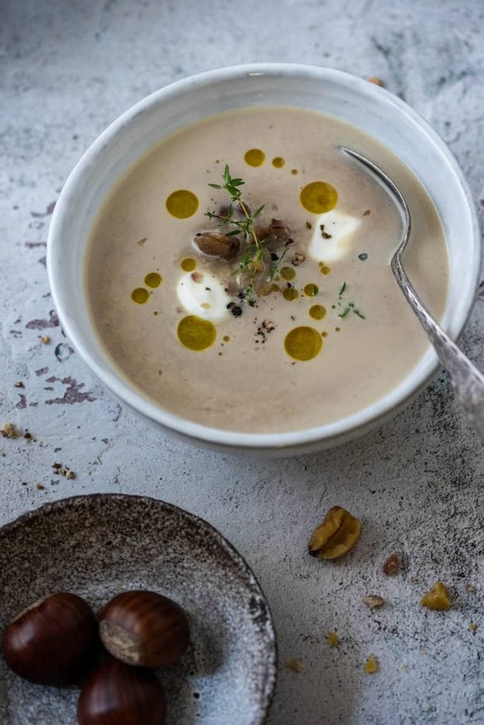 Cremige Maronensuppe in einer Suppenschale mit Edelkastanien daneben.