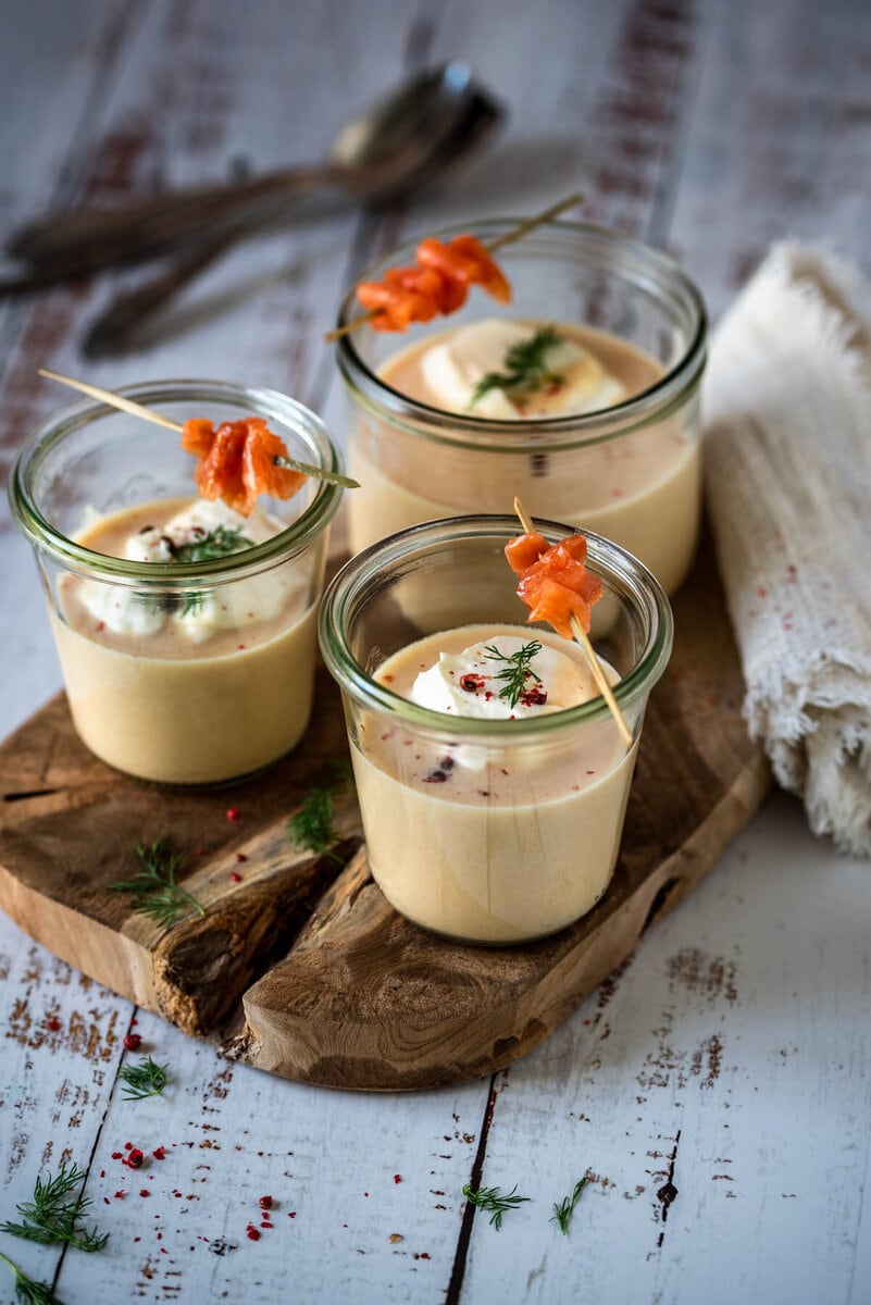 3 Gläser mit Cremesuppe vom Räucherlachs stehen auf einem Holzbrett