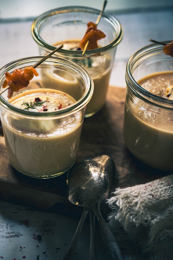 3 Gläser mit Cremesuppe vom Räucherlachs stehen auf einem Holzbrett