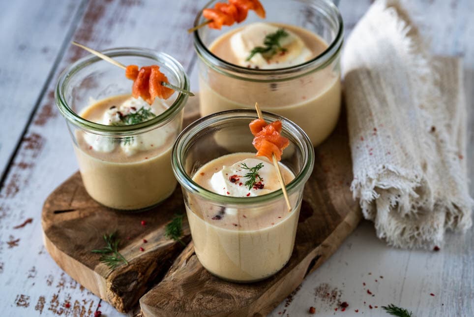 3 Gläser mit Cremesuppe vom Räucherlachs stehen auf einem Holzbrett
